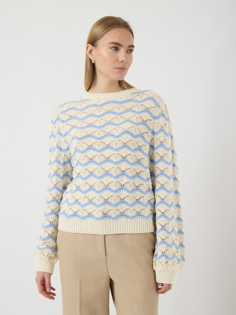 Pull en tricot léger de couleur crème avec un motif en zigzag bleu, des poignets et un ourlet côtelés, et une texture au maillage ouvert.