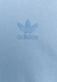 Blue knit fabric with a subtle embossed Adidas trefoil logo and brand name centered on the surface.