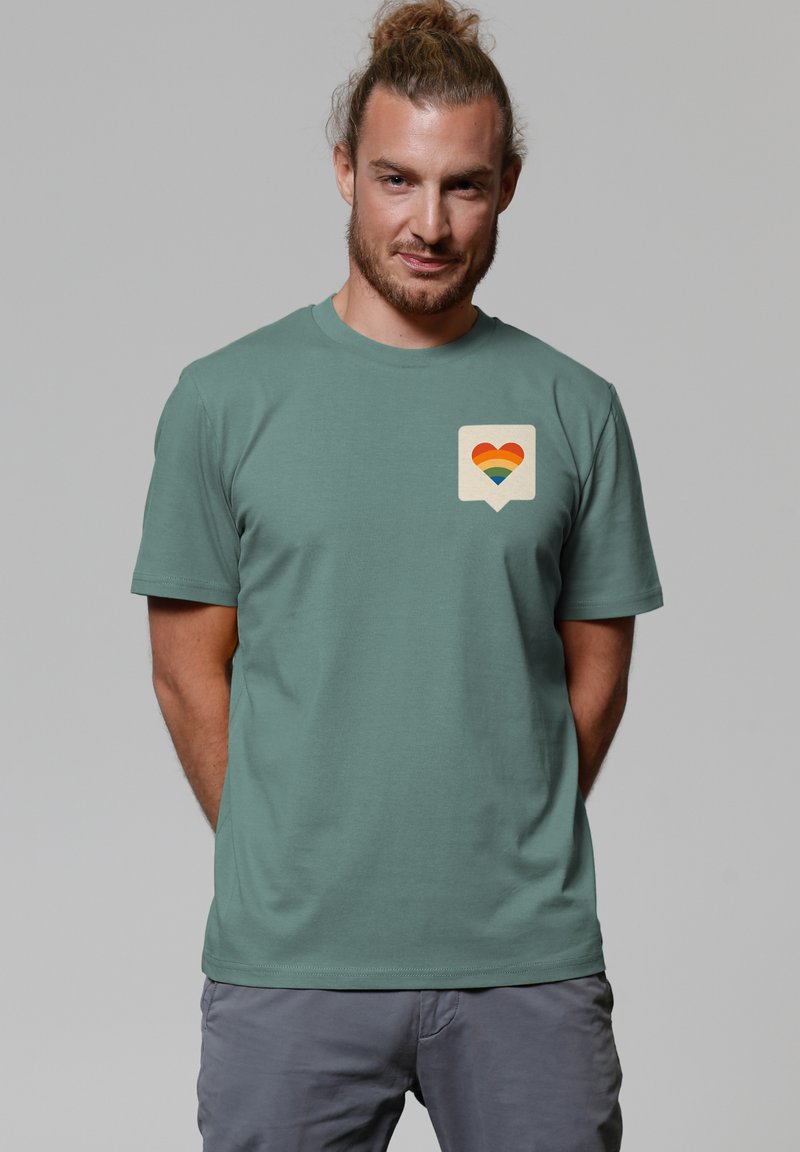 Lichtgroene katoenen t-shirt met een hartgrafiek in regenboogkleuren op een crèmekleurige spraakbel, korte mouwen, ronde halslijn.