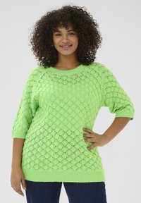 Heldere groene gebreide trui met een ruitpatroon, ¾ mouwen, ronde halslijn en geribbelde boorden en zoom. Gecombineerd met donkerblauwe jeans.