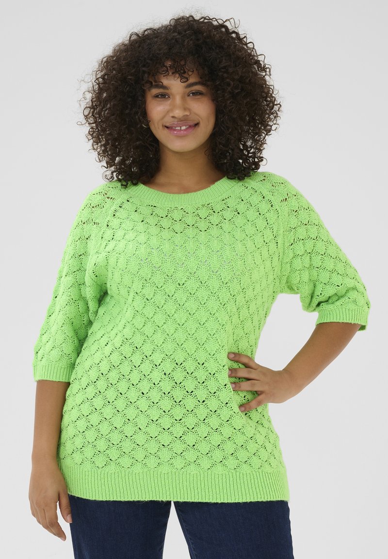 Heldere groene gebreide trui met een ruitpatroon, ¾ mouwen, ronde halslijn en geribbelde boorden en zoom. Gecombineerd met donkerblauwe jeans.