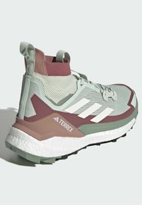 Vihreä urheilukenkä korkealla varrella, valkoisilla yksityiskohdilla ja teksturoiduilla yksityiskohtilla. Varustettu pehmustetulla pohjalla ja kuviollisella neulepäällä.