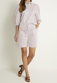 Top in tessuto leggero a righe con chiusura a bottoni, abbinato a pantaloni corti coordinati. Sandali con tacco marroni completano l'outfit.