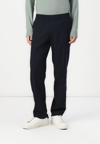 Navy trousers with an elastic waistband, tailored fit, and side pockets, paired with white sneakers and a light green sweater.