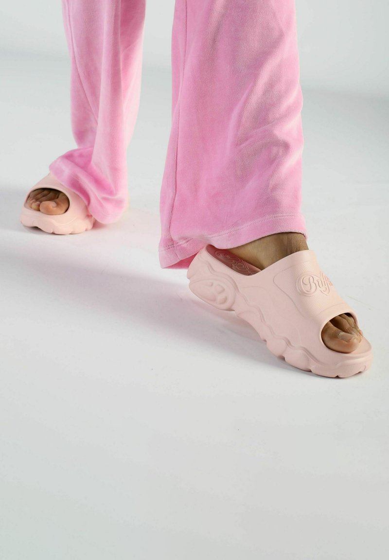 Rosa gummisandaler med öppen tå-design, texturerad ovandel och en vågig sula, tillsammans med matchande lösa rosa byxor.