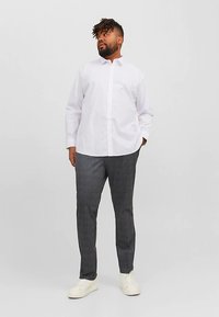 Balti marškiniai su ilgomis rankovėmis, pilkos spalvos languoti kostiuminės kelnės ir balti sportbačiai. Marškiniuose yra standartinis apykaklės dėžutės tipo apykaklė; kelnės aptemptos.