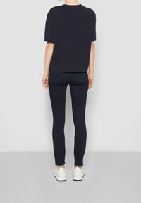 Camiseta de manga corta azul marino combinada con vaqueros ajustados azul oscuro y zapatillas blancas. El conjunto presenta un corte relajado y un diseño minimalista.