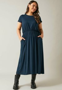 Granatowa sukienka midi z krótkimi rękawami, elastycznym pasem i kieszeniami bocznymi. Noszona z czarnymi botkami do kostek. Gładki, lekki materiał.