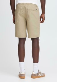 Beige shorts med en afslappet pasform, elastisk talje og to baglommer. Kombineret med hvide crew-sokker og lysebrune sneakers.