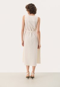 Mouwloze, crèmekleurige midi-jurk met een gestructureerd patroon, een getailleerde taille en zijslits. Gepaard met strappy hakken voor een evenwichtige uitstraling.
