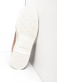 Zapatilla de lona con parte superior de color rosa claro y suela de goma blanca. La suela texturizada presenta patrones en zigzag y un estampado de logo.
