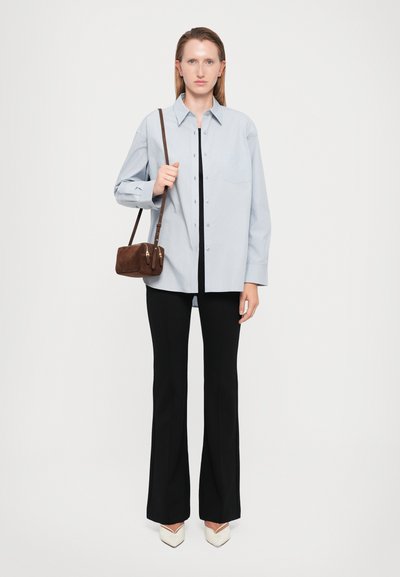 Hellblaues Hemd mit Knöpfen, schwarze Hose, weiße Absatzschuhe und eine kleine braune Handtasche mit Schulterriemen.