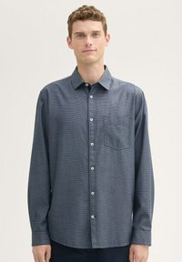 Camisa de manga larga abotonada en azul marino. Tela texturizada con un bolsillo en el pecho izquierdo. Cuenta con un cuello estándar y botones blancos.
