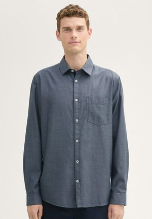 Camisa de manga larga abotonada en azul marino. Tela texturizada con un bolsillo en el pecho izquierdo. Cuenta con un cuello estándar y botones blancos.