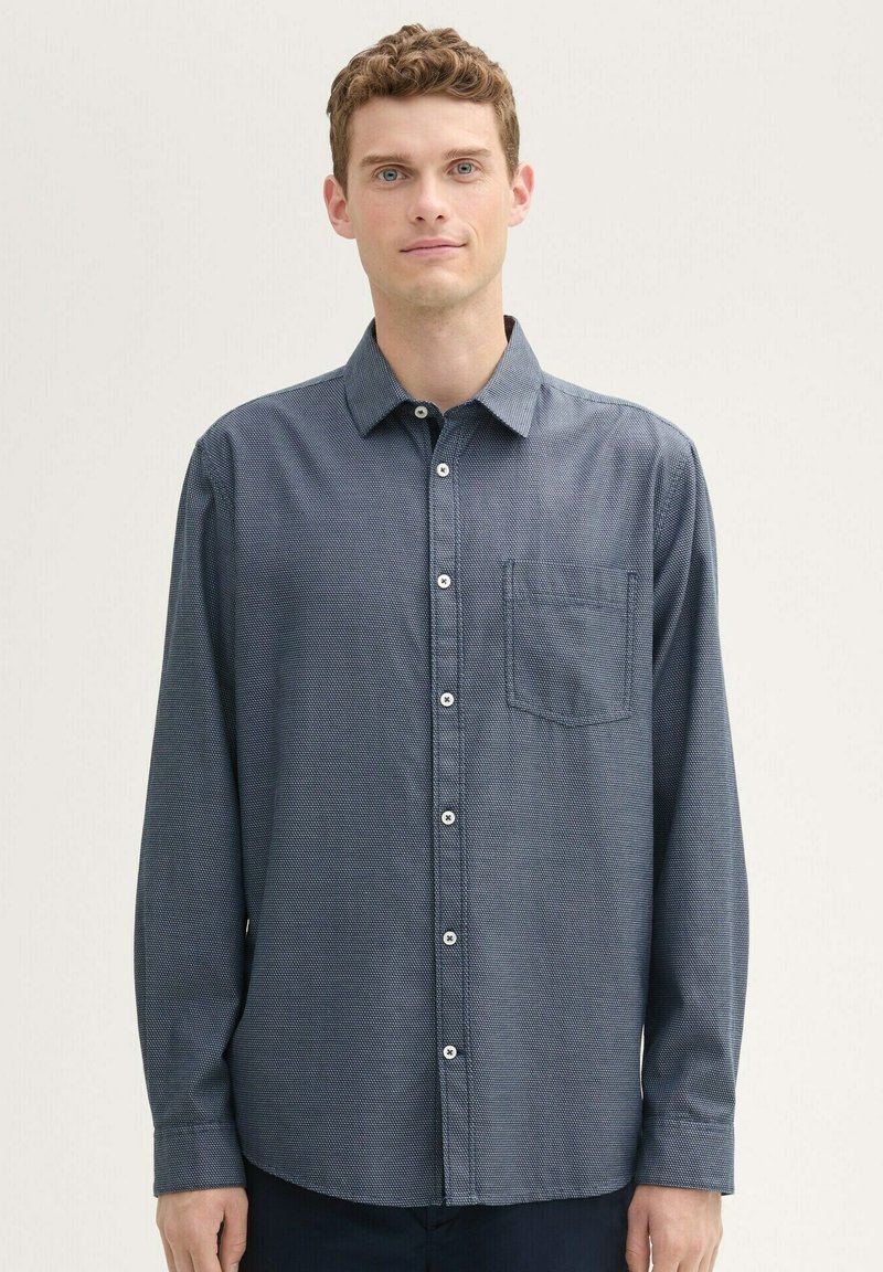 Long-sleeve button-up shirt in navy blue. Textured fabric with a pocket on the left chest. Features a standard collar and white buttons.