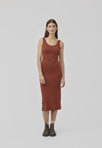 Robe midi sans manches rouge à rayures avec un col arrondi ; coupe ajustée ; associée à des bottes marron jusqu'à la cheville et des chaussettes de couleur claire.
