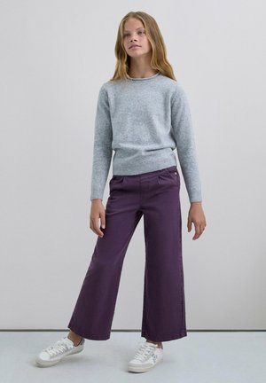 Jersey de punto gris claro con cuello redondo y puños acanalados, combinado con pantalones morados de pierna ancha y zapatillas blancas con detalles grises.