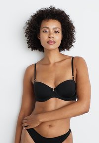 Black underwire bra with smooth fabric, contoured cups, adjustable straps, and a minimal design. Worn with matching black briefs.