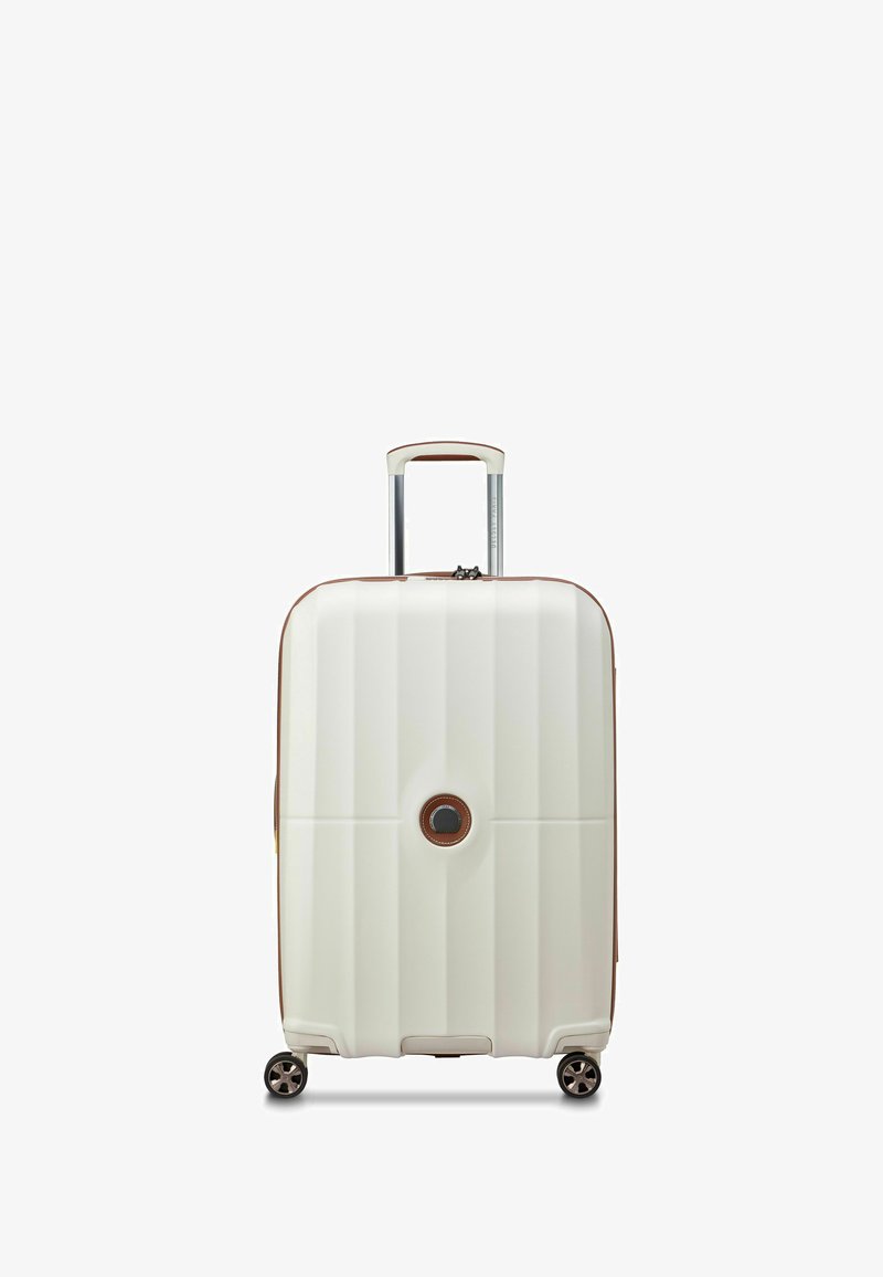 Valise rigide blanche avec des rainures verticales, des accents marron, une poignée rétractable et quatre roues noires. Logo rond au centre.