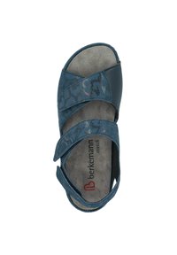 Blue sandal with cross straps, featuring a floral pattern, soft suede insole, and adjustable closure. Brand name visible on insole.