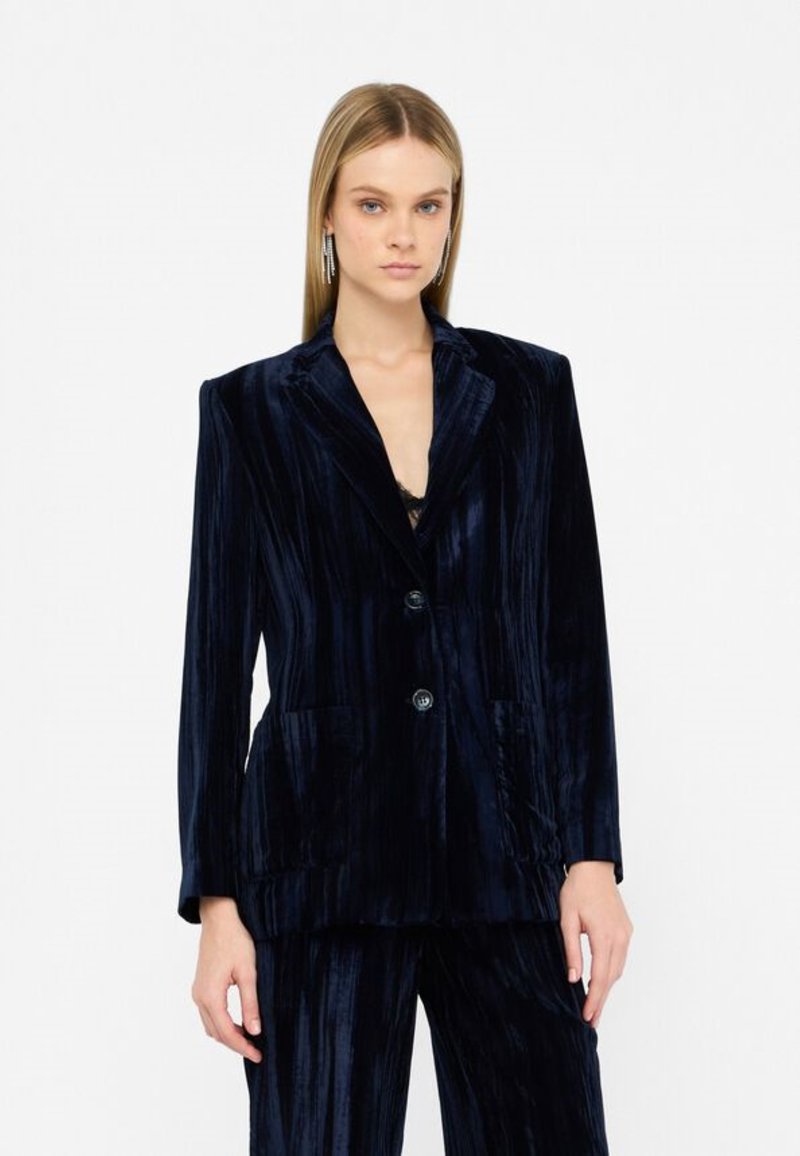 Blazer de terciopelo azul marino con rayas verticales, dos bolsillos frontales y cierre de dos botones. Textura suave con brillo pronunciado.