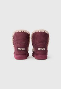 Stivali alla caviglia in suede viola del marchio Mou, con cuciture color crema e foderato in shearling, caratterizzati da una suola piatta e un dettaglio con logo.