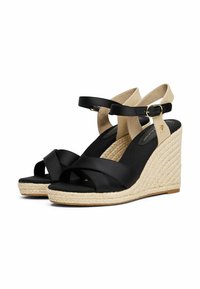Sandales compensées noires avec une semelle en jute tissée. Présente des brides croisées à l'avant, une bride de cheville réglable et un revêtement en tissu doux.