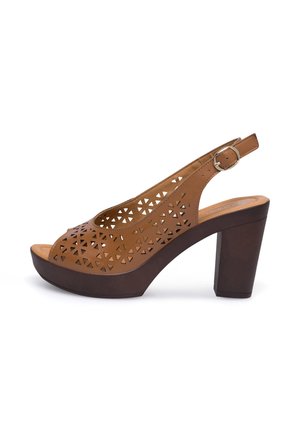 Brązowe, perforowane skórzane sandały na wysokim obcasie z zapięciem na pięcie i grubą platformą. Posiadają geometryczne wycięcia oraz gładką fakturę.
