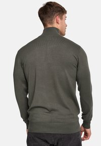 Donkergroen gebreid sweater met een hoge kraag, een getailleerd ontwerp, geribbelde manchetten en zoom, en een gladde textuur, getoond vanaf de achterkant.