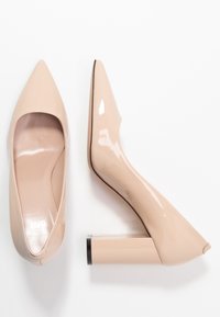 Escarpins en cuir verni nude avec un bout pointu et un talon carré épais. Texture lisse avec une finition brillante et un design minimaliste.