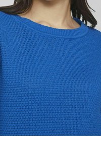 Blå texturerad tröja med rund hals och ribbade ärmslut. Tyget har ett våffelmönster som ger ett mjukt och andningsbart utseende.