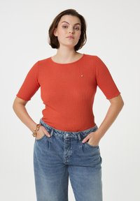 Geribbelde, korte mouwen top in oranje, met een ronde halslijn en een klein hartlogo. Gepaard met losse, lichtblauwe denim jeans.