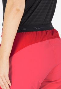 Röda sportshorts med svart midjeband, med slätt tyg och en tät passform, visade från sidan.