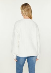 Pulover alb din tricotaj cu model cable-knit, guler rotund și mansete cu model din jerseu, având o croială lejeră și un model texturat, asociat cu blugi albaștri.