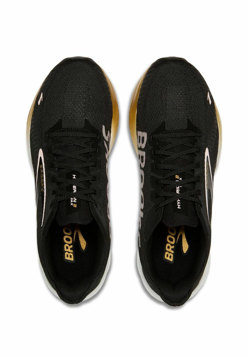 Schwarze Sportschuhe mit einem Obermaterial aus Mesh, weißen und goldenen Akzenten, auffälligem Schnürsystem und gebrandeten Einlegesohlen. Die Außensohlen weisen ein strukturiertes Design auf.