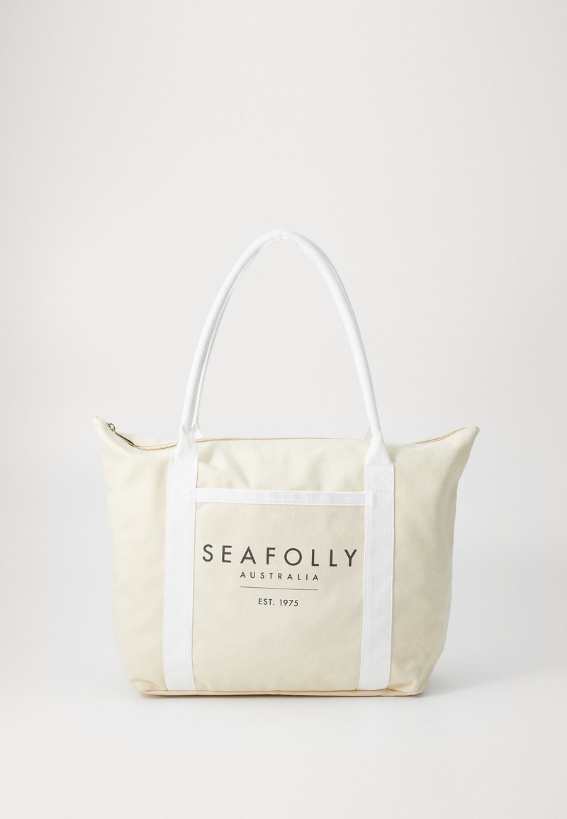 Kanvas torba v smetani z belimi ročaji. Ima sprednji žep z logotipom "SEAFOLLY AUSTRALIJA" in zadrgo na vrhu.