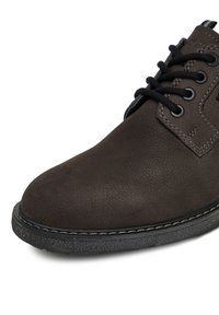 Tmavě hnědá kožená bota s texturovaným povrchem, zaoblenou špičkou, černými tkaničkami a kontrastním bílým prošíváním podél podešve.