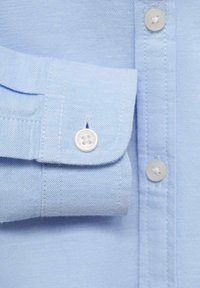 Vaaleansininen kauluspaita, jossa on valkoiset napit, sileä pinta ja huolellisesti ommellut saumat.