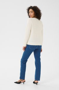 Pull en tricot blanc avec ourlet à côtes, associé �à un jean droit en denim bleu. Le modèle porte des escarpins noirs à bride arrière, vu de l'arrière.