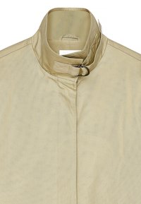 Bežs bez apkakles žakets ar gludu tekstūru, ar priekšējo aizdari, regulējamu cilpu un smalkiem šuvju elementiem.