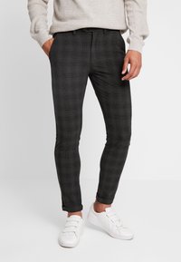 Smalpassande, mörkgrå rutiga byxor med en slät tygtextur, uppvikta fållar och en platt frontdesign, kombinerade med vita sneakers.