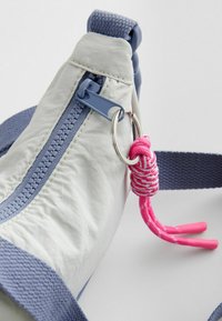 Borsa in tessuto grigio chiaro con cerniera blu, dotata di manico in corda rosa. Caratterizzata da una superficie testurizzata e da una tracolla blu in contrasto.