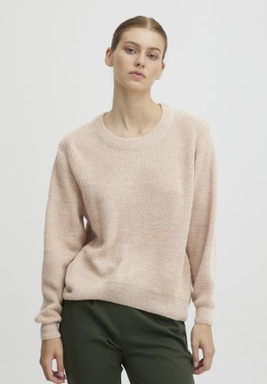Pull en tricot rose clair avec un col rond côtelé et des manches longues. Présente une coupe décontractée et un tissu texturé. Associé à un pantalon vert foncé.