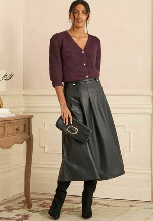 Fioletowy sweter z dzianiny z krótkimi rękawami i detalami w postaci guzików, w połączeniu z czarną plisowaną spódnicą ze skóry i czarnymi botkami na obcasie.