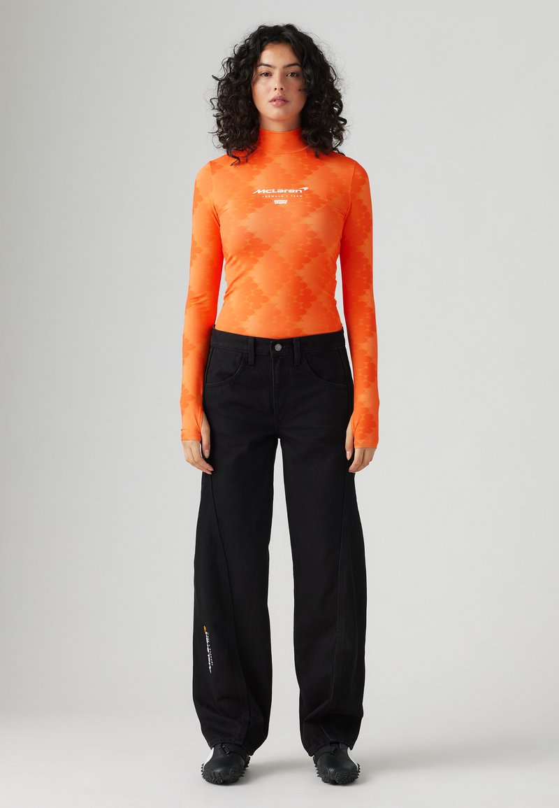 Orange long-sleeve top with a diamond pattern and logo; paired with black wide-leg jeans. The outfit features textured fabric and casual shoes.