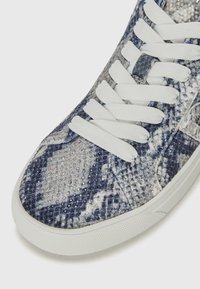 Scarpe sportive con un design a stampa serpente blu e bianco, tomaia testurizzata e lacci bianchi. Suola in gomma con un battistrada decorato per una migliore aderenza.