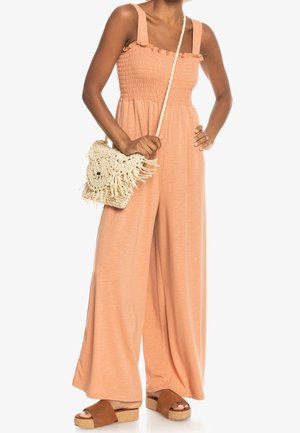 Ferskenfarvet jumpsuit med smocket bodice, brede ben og flæse-stropper. Sættes sammen med en vævet taske med frynser og brune plateau-sandaler.