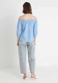 Ljusblå off-shoulder topp med volangkant, långärmad och loose fit, kombinerad med högmidjade ljusblå jeans.