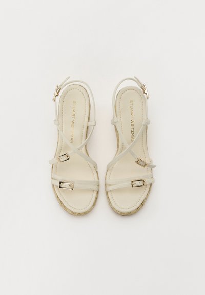 Två krämfärgade sandaletter med remmar i strappy-stil har tunna remmar och spännen med en texturerad plattformssula. Det inre foder är slätt och vadderat.