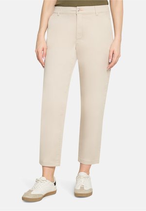 Beżowe spodnie chinos o prostych nogawkach, z zapięciem na guzik i przednimi kieszeniami, w połączeniu z białymi i beżowymi trampkami.